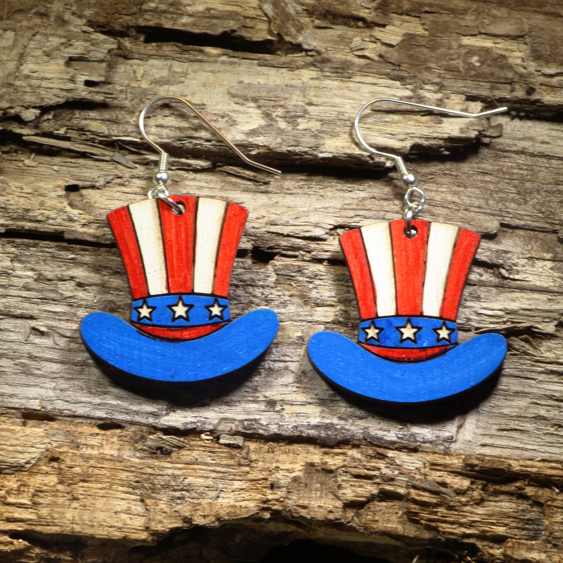 Hand-painted wooden Uncle Sam hat dangle earrings featuring the classic red, white, and blue stars-and-stripes top hat inspired by the iconic symbol of American patriotism. Crafted from lightweight wood with hypoallergenic .925 sterling silver hooks, these festive earrings are perfect for Independence Day, Fourth of July celebrations, Memorial Day, Veterans Day, patriotic events, Americana fashion, and anyone who loves showing their American pride.