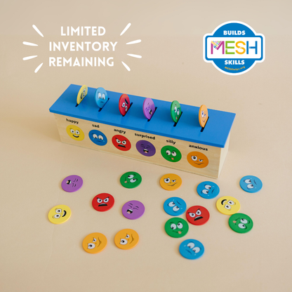 Emotions sorting game with colorful emotion coins and a wooden box on a beige background, featuring &