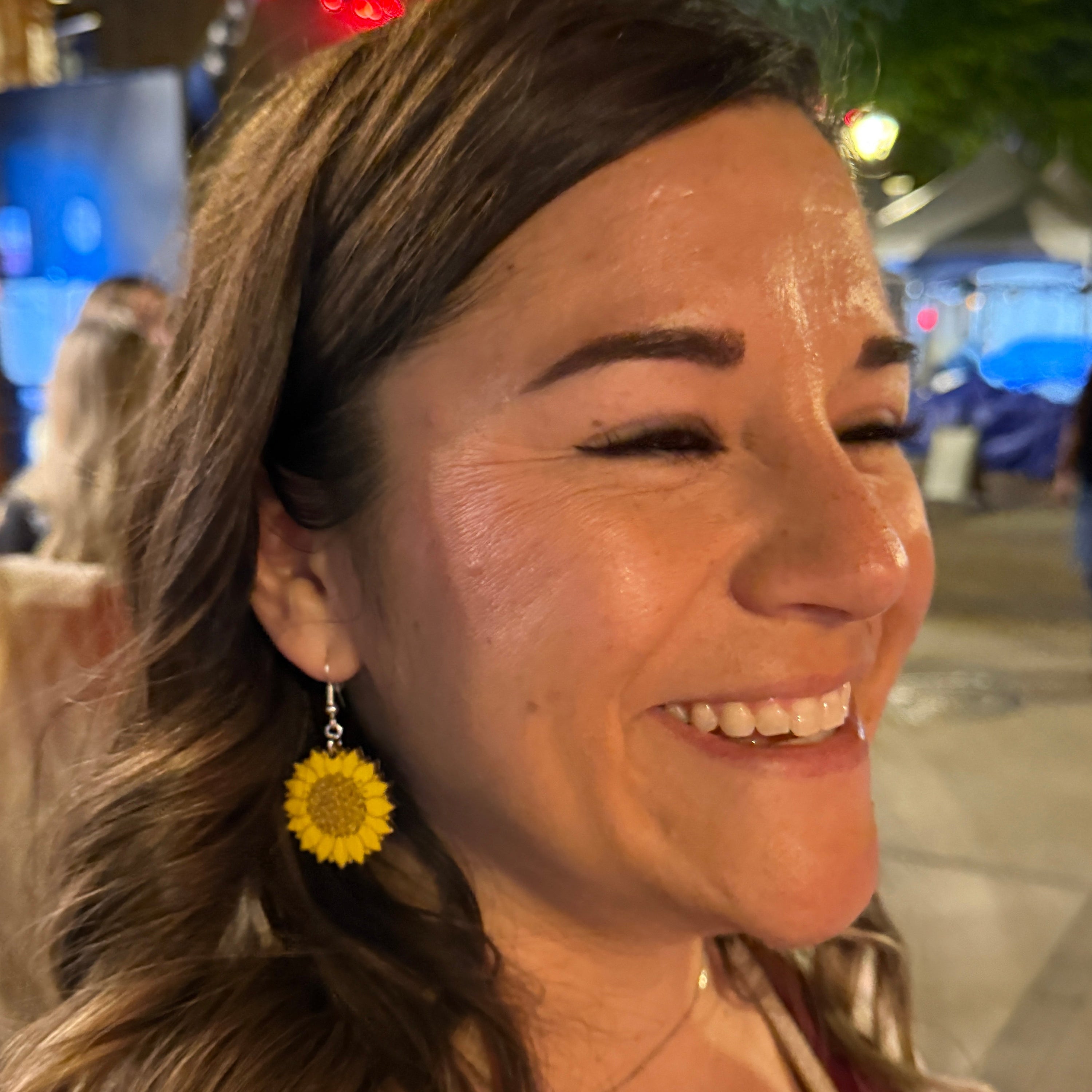 Woman wearing hand-painted wooden sunflower dangle earrings featuring a bright yellow sunflower with a detailed brown center. This lifestyle photo showcases the size and lightweight comfort of these handmade wooden earrings with hypoallergenic .925 sterling silver hooks, perfect for sunflower lovers, country style, fall fashion, summer outfits, and nature-inspired jewelry.