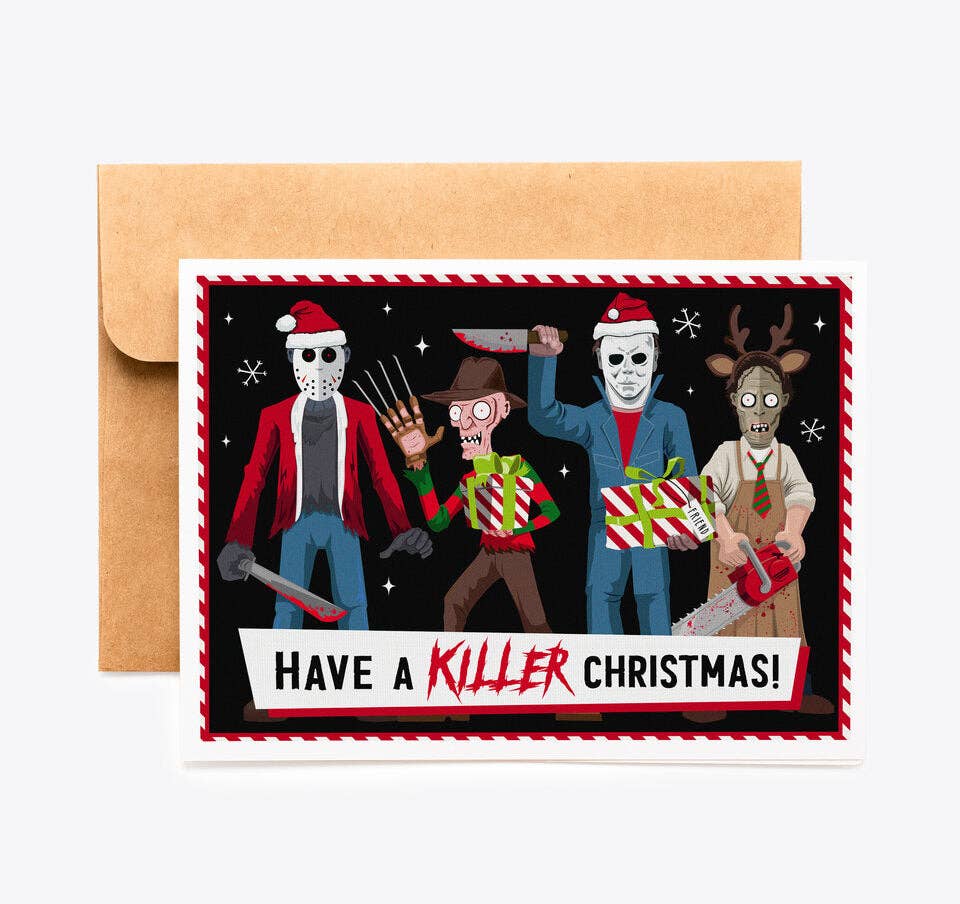 A horror-themed Christmas greeting card with a kraft paper envelope behind it, featuring illustrated characters in holiday costumes holding weapons on a black background with the text &