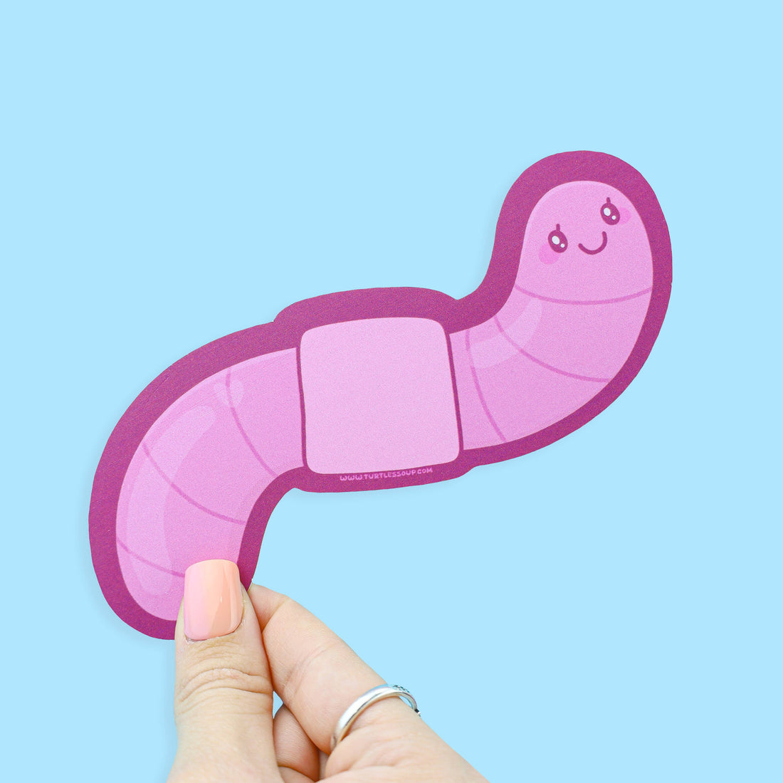 Hand holding a pink caterpillar-shaped sticker against a light blue background
