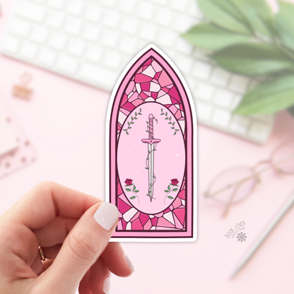 Pink stained glass-style sticker with a sword and roses held by a hand on a light background.