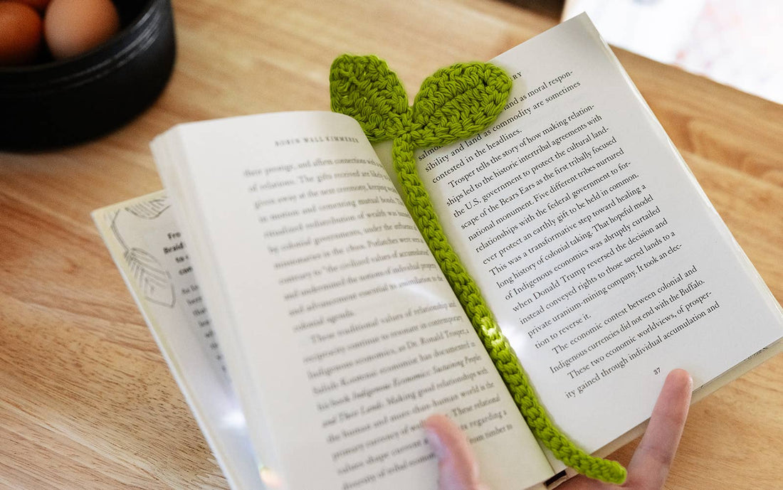 Open book with a green crocheted bookmark on a wooden surface