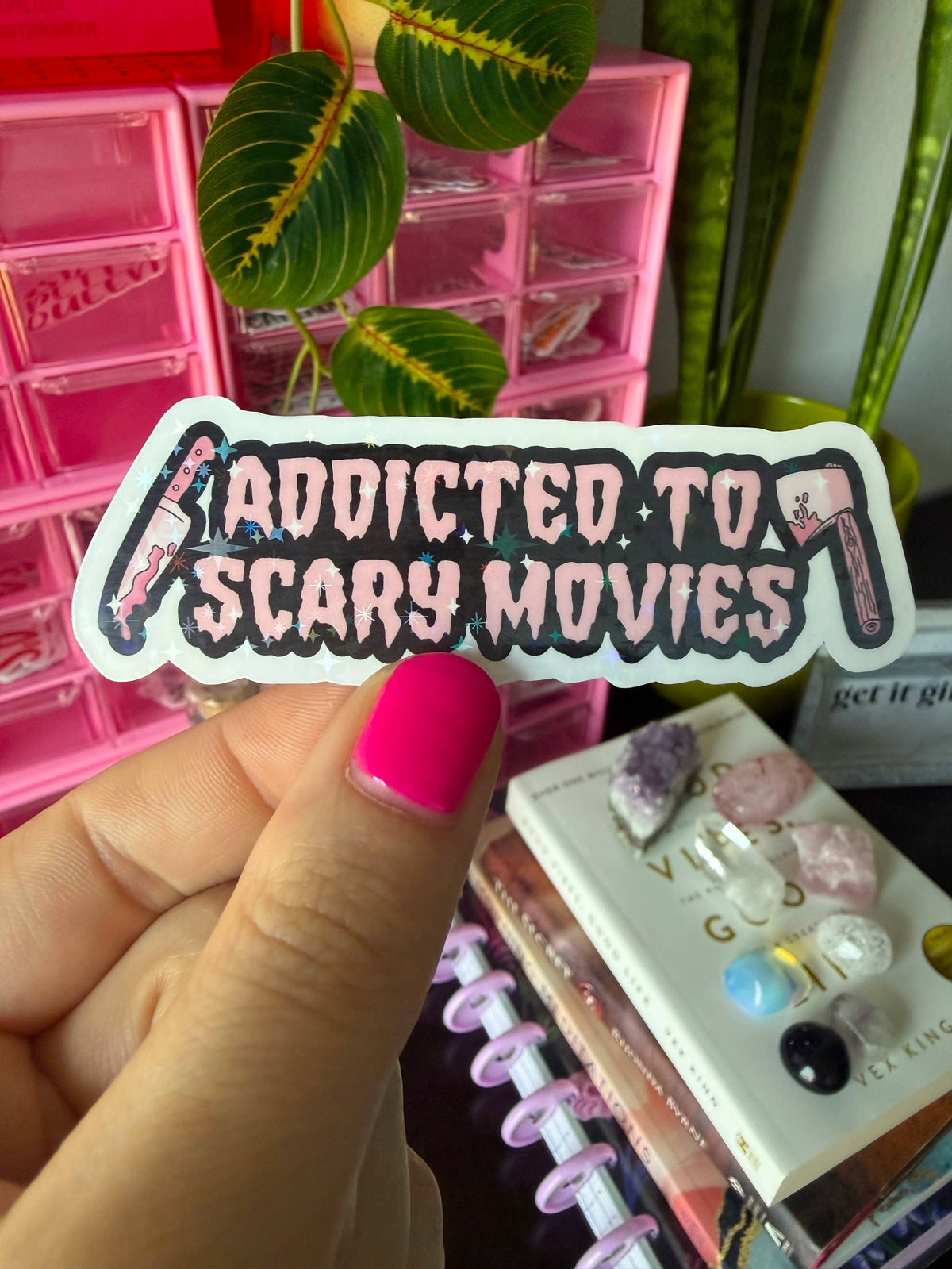 A hand with bright pink nail polish holds a die-cut sticker that reads &