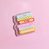 A clear plastic object with colorful bandages and text on it, placed on a pink background.