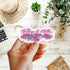 A hand holds a die-cut sticker featuring a pink and purple dagger surrounded by roses with the phrase &