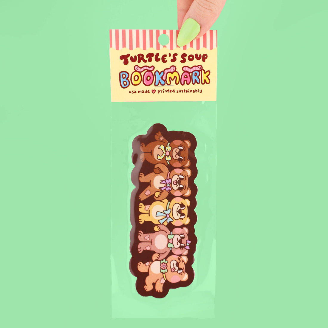 Bookmark with cartoon teddy bear design held by a hand against a green background