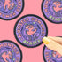 A circular sticker with a purple and pink monster illustration and the words &