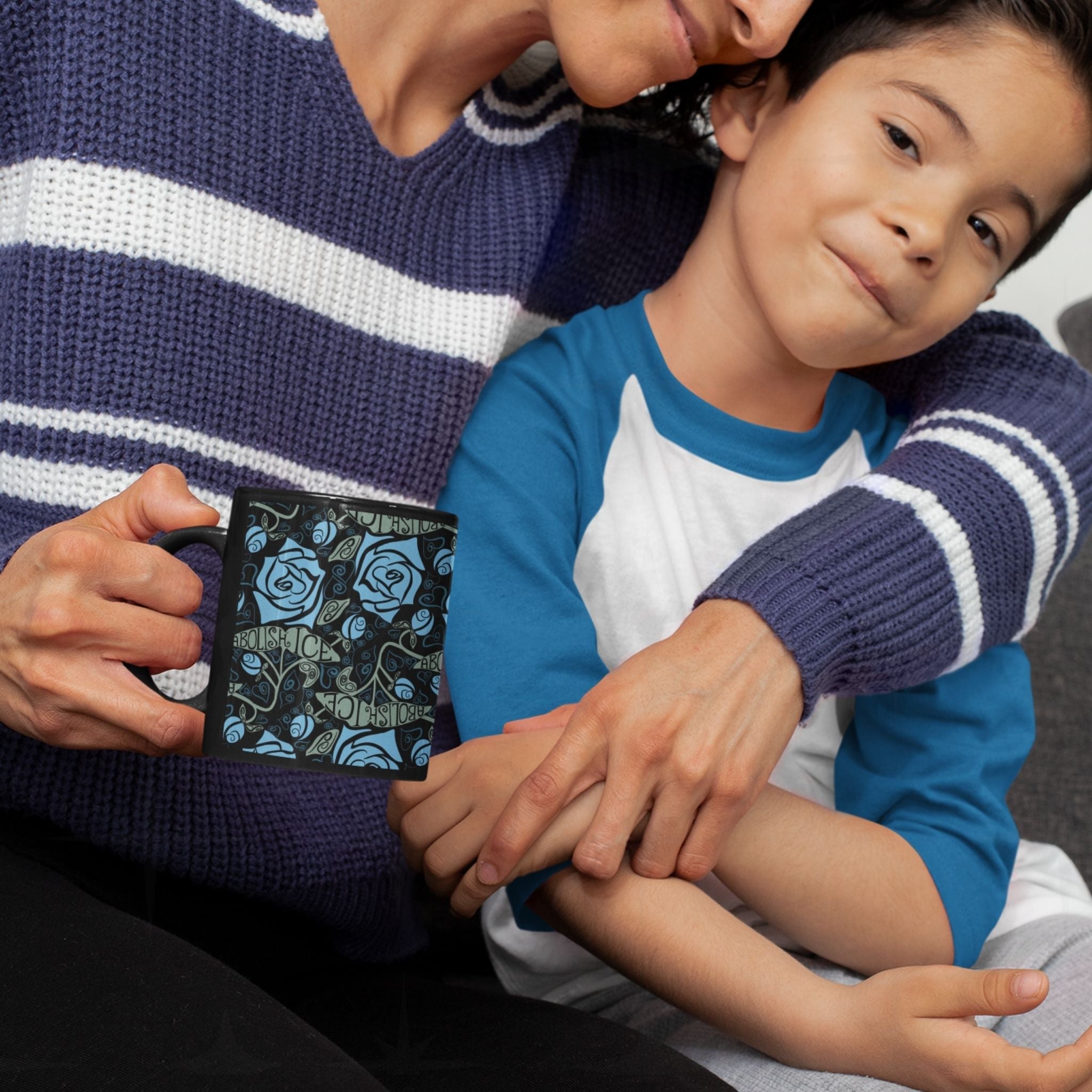 Adult holding the Abolish ICE mug while embracing a child, black ceramic gothic rose wrap print, warm lifestyle moment