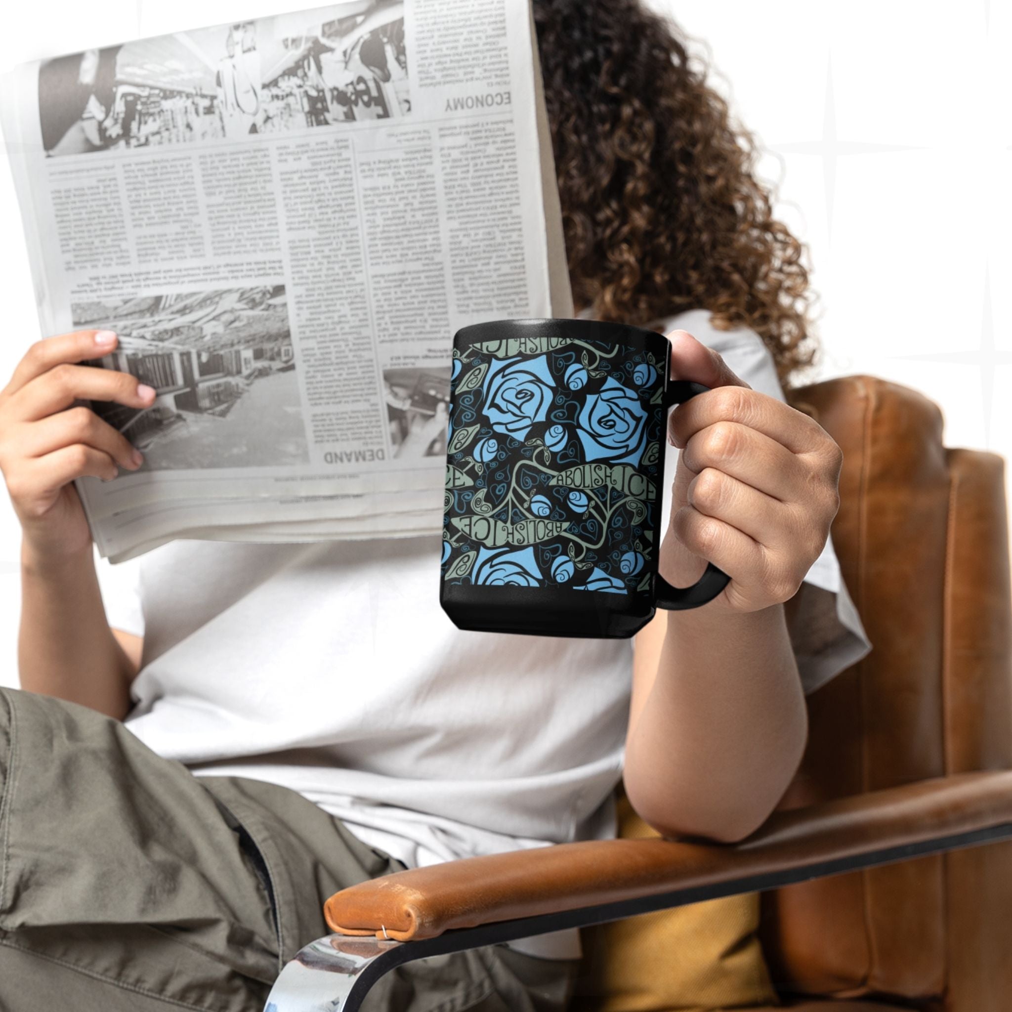 Person reading a newspaper and holding the Abolish ICE coffee mug, black ceramic with gothic blue rose wrap print