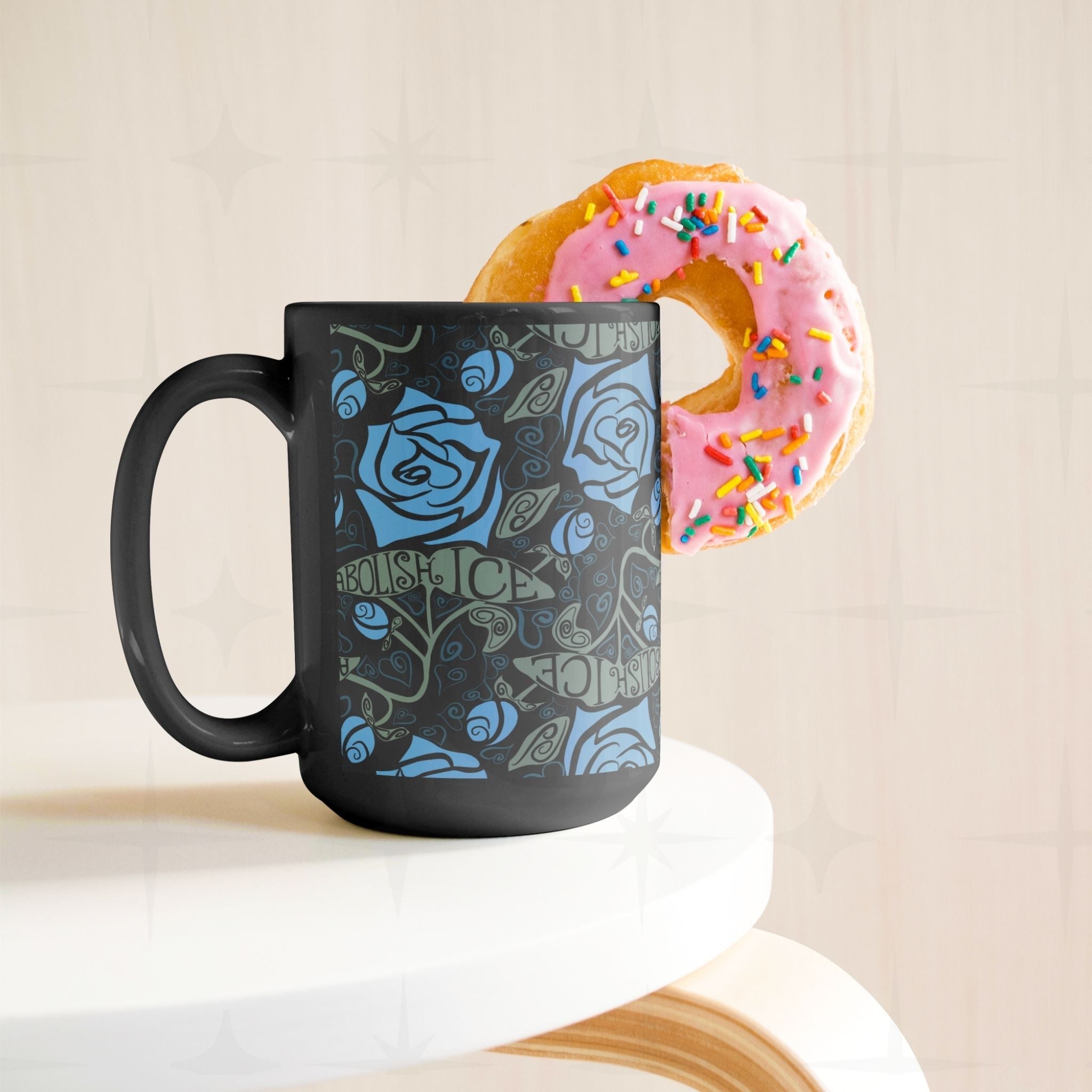 Abolish ICE coffee mug on white surface styled with a pink sprinkle donut, black ceramic gothic rose wrap print