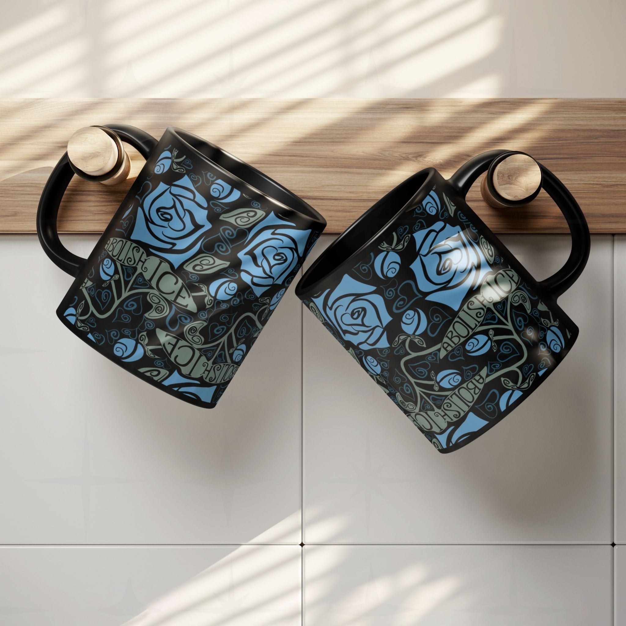 Two Abolish ICE mugs balanced on a kitchen ledge, overhead view showing blue rose and sage-green banner wrap print