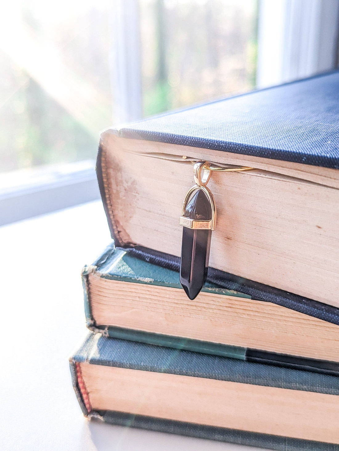 Black crystal pendant on a stack of books with a blurred window background