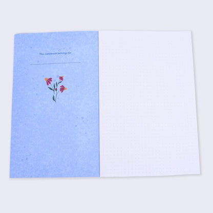 open flat lay notebook with dot grid pages and blue inside cover has a small flower illustration and text "this notebook belongs to"