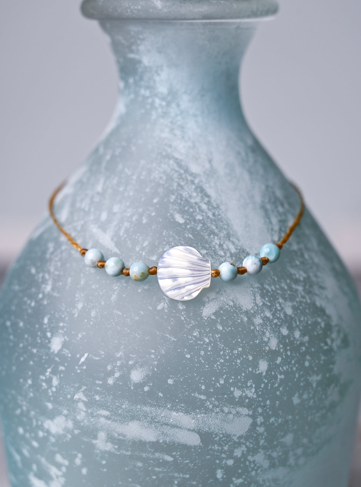 Close up view of a scallop shell and larimar beaded ankle bracelet on a blue vase.