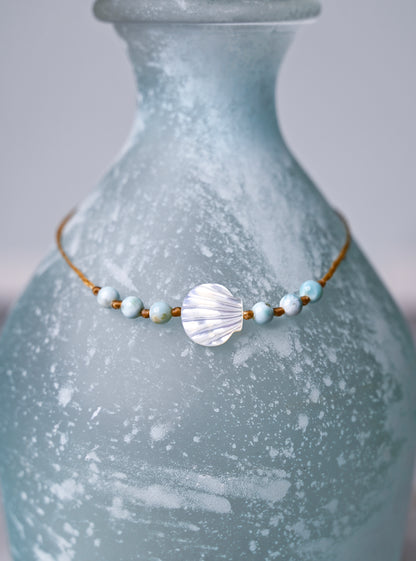 Close up view of a scallop shell and larimar beaded ankle bracelet on a blue vase.