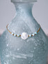 Close up view of a scallop shell and larimar beaded ankle bracelet on a blue vase.