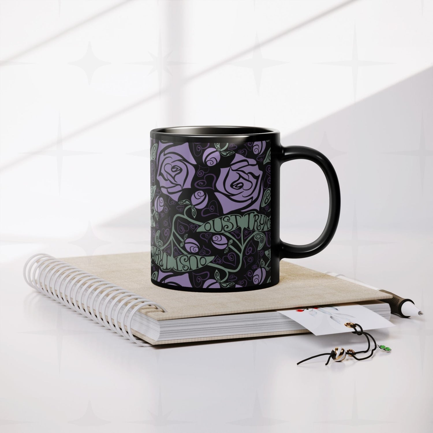 Anti-Trump hidden message black ceramic mug resting on spiral notebook with pen and accessories