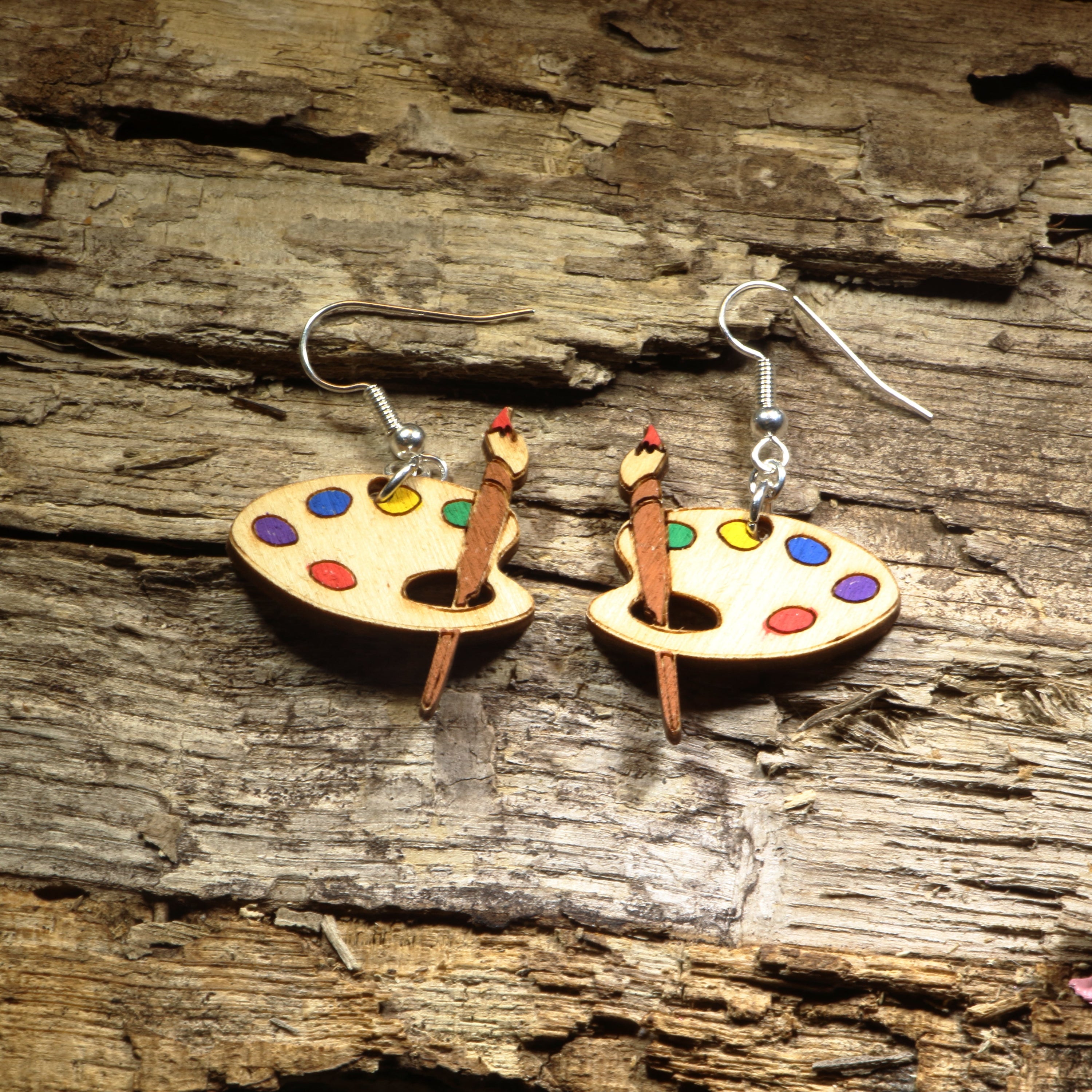Hand-painted wooden artist palette dangle earrings featuring a classic paint palette with colorful paint spots and a detailed paintbrush. Crafted from lightweight wood with hypoallergenic .925 sterling silver hooks, these creative earrings are perfect for artists, painters, art teachers, art students, creative professionals, and anyone who loves unique art-inspired jewelry.