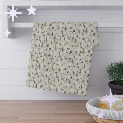 Warm gray atomic starburst cotton twill kitchen towel hanging from a round chrome hook against bright white subway tile with wooden shelves and stacked plates visible