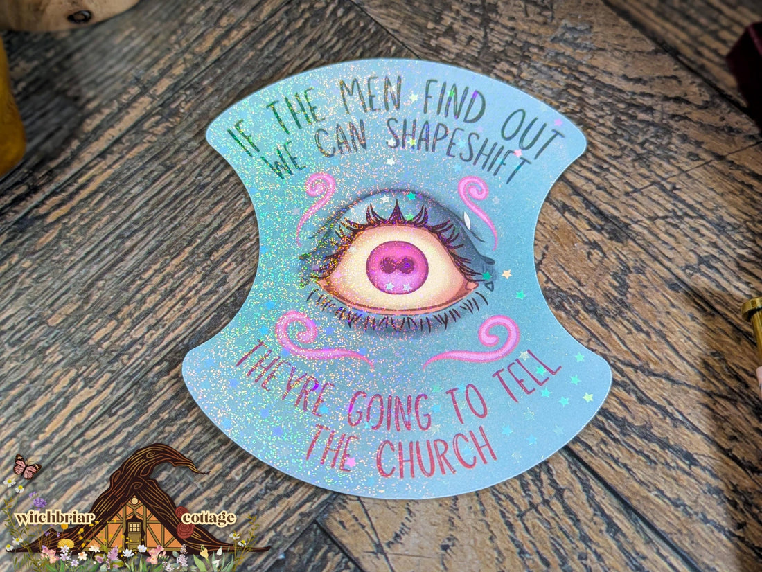 Decorative eye-shaped card with text on a wooden surface, featuring the brand &