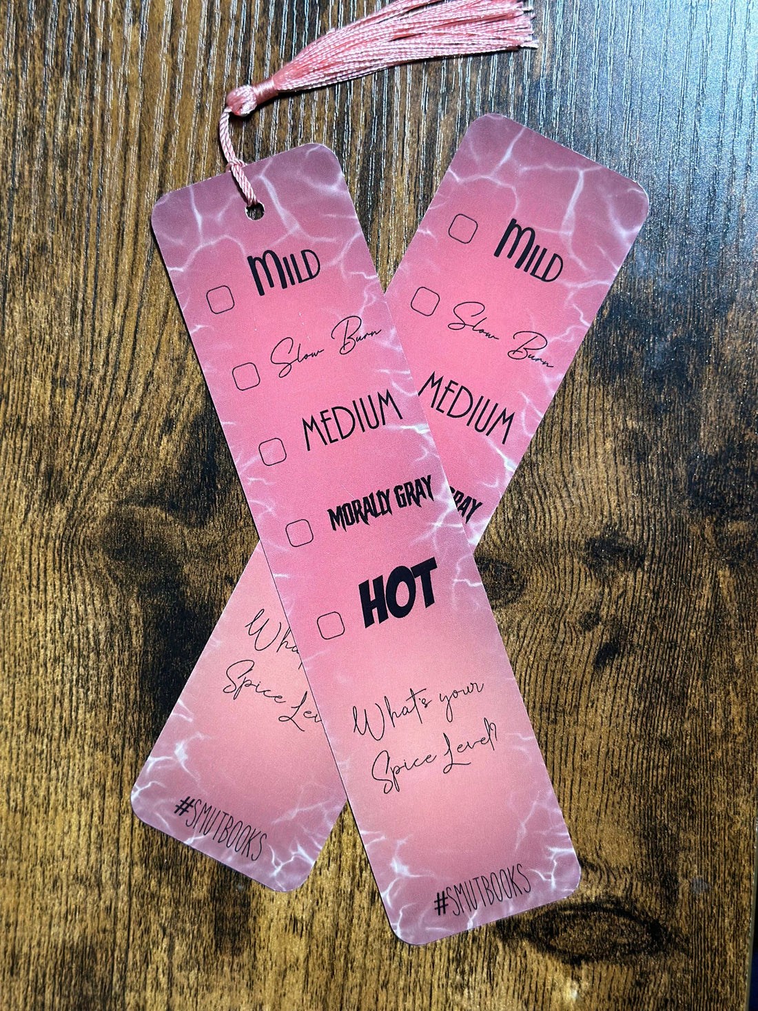 Two pink marbled bookmarks with text on a wooden surface