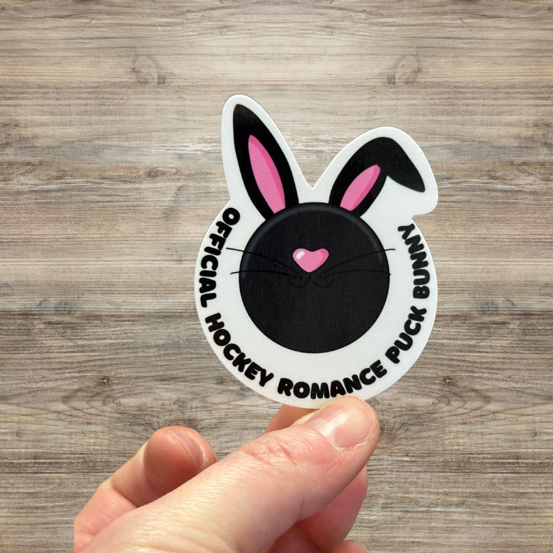 Sticker with bunny ears and text held by a hand on a wooden surface