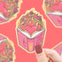 Sticker of an open book with a heart and romance theme held by a hand against a red background.