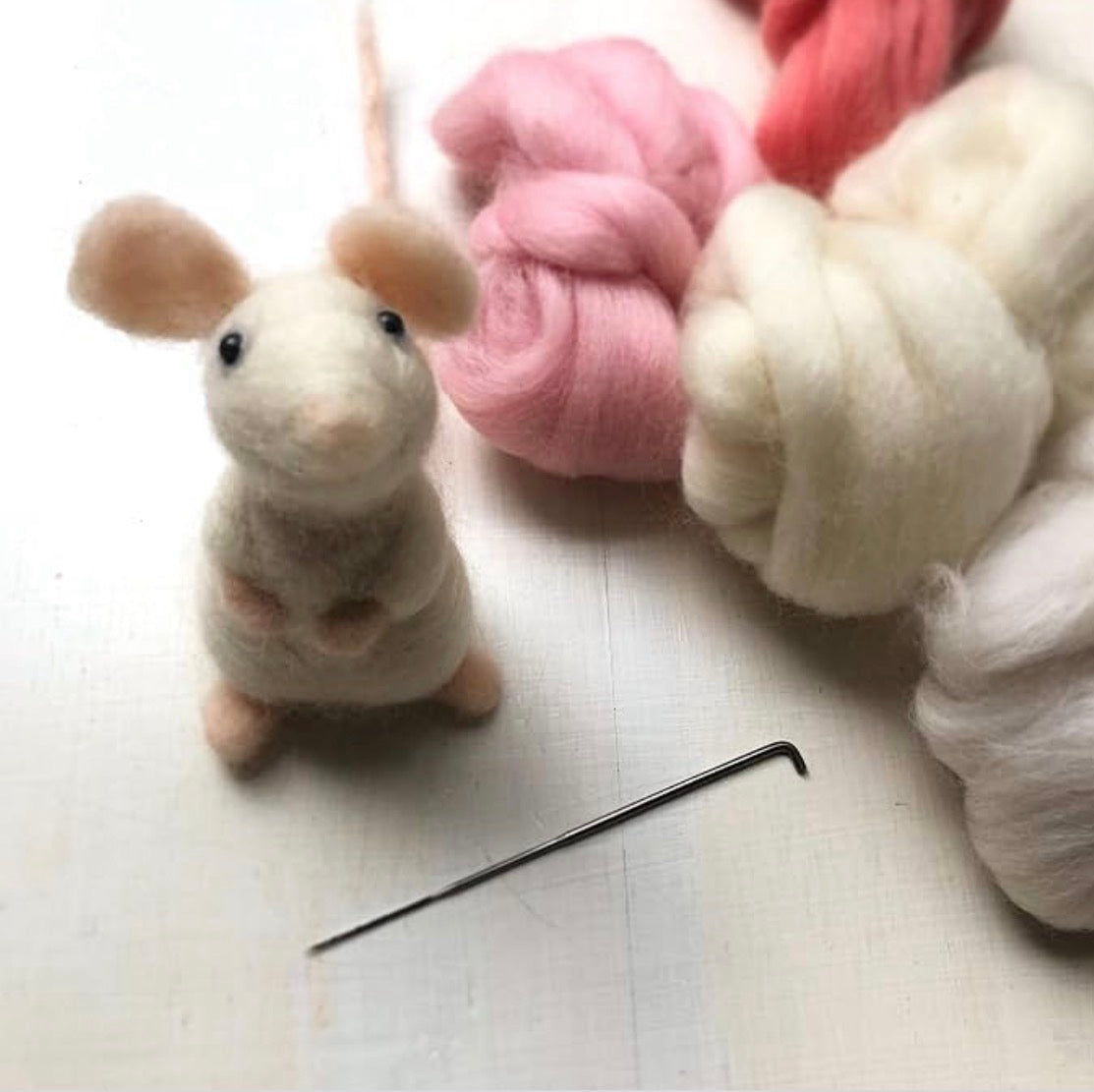 Close-up of a finished needle-felted mouse next to pastel merino wool fibres
