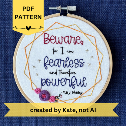 PDF pattern created by Kate, not AI. "Beware; for I am fearless and therefore powerful - Mary Shelley". Quote hand embroidered in dark red, black, and deep royal blue. Framed in yellow and orange hexagon wreaths with floral bundle on the bottom left. Gold stars sparkle on the sides. Fabric is white-on-white cotton. Displayed as wall art in a light wooden embroidery hoop.