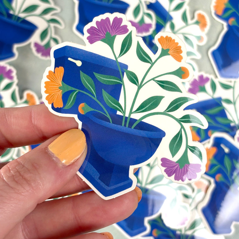 hand holding A sticker depicting a toilet bowl filled with colorful flowers