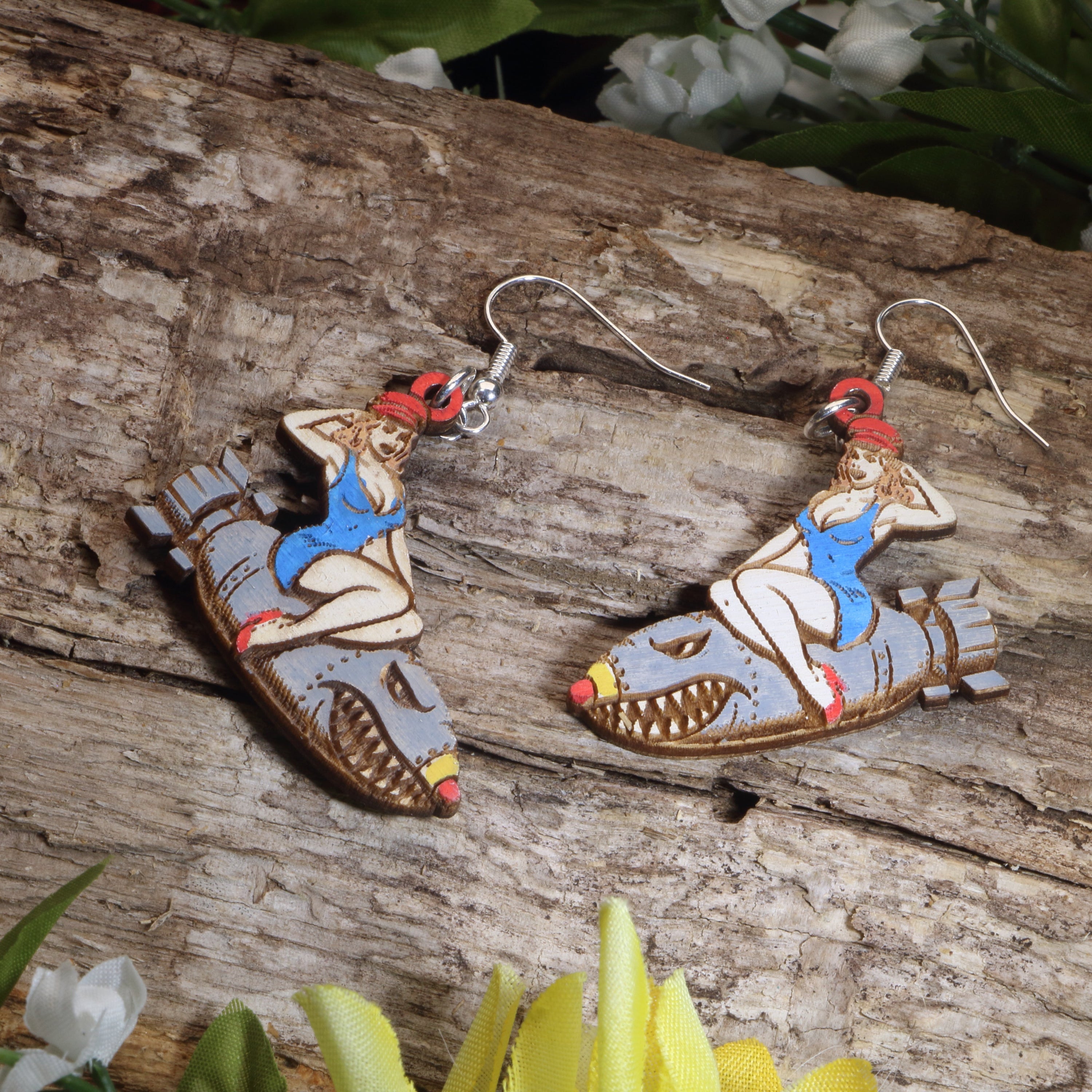 Hand-painted wooden bomber girl dangle earrings featuring a vintage pin-up riding a shark-mouth bomber design, hypoallergenic sterling silver hooks, and lightweight retro military-inspired jewelry for aviation enthusiasts and WWII nostalgia lovers by Cate’s Concepts.
