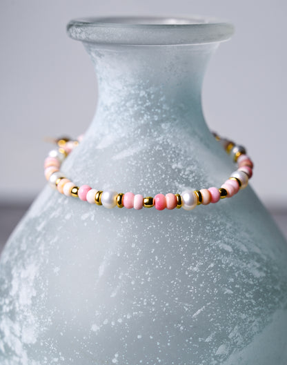 A closeup view of a pink shell bracelet with gold accents.