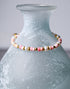 A closeup view of a pink shell bracelet with gold accents.