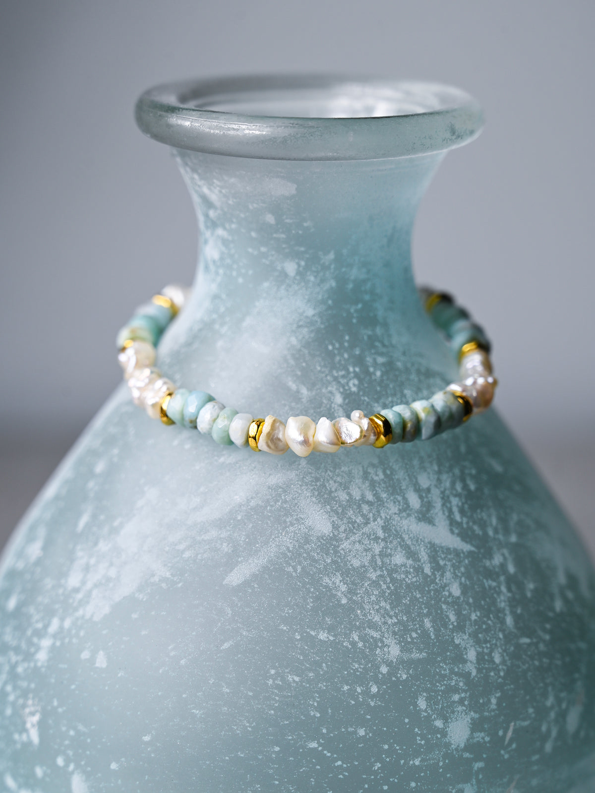 A close up view of a larimar and pearl nugget stretch bracelet with gold accents.
