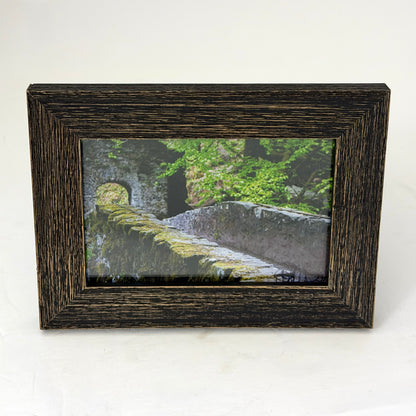 framed print of a stone bridge in a forest in the scottish highlands in a weathered style brown frame
