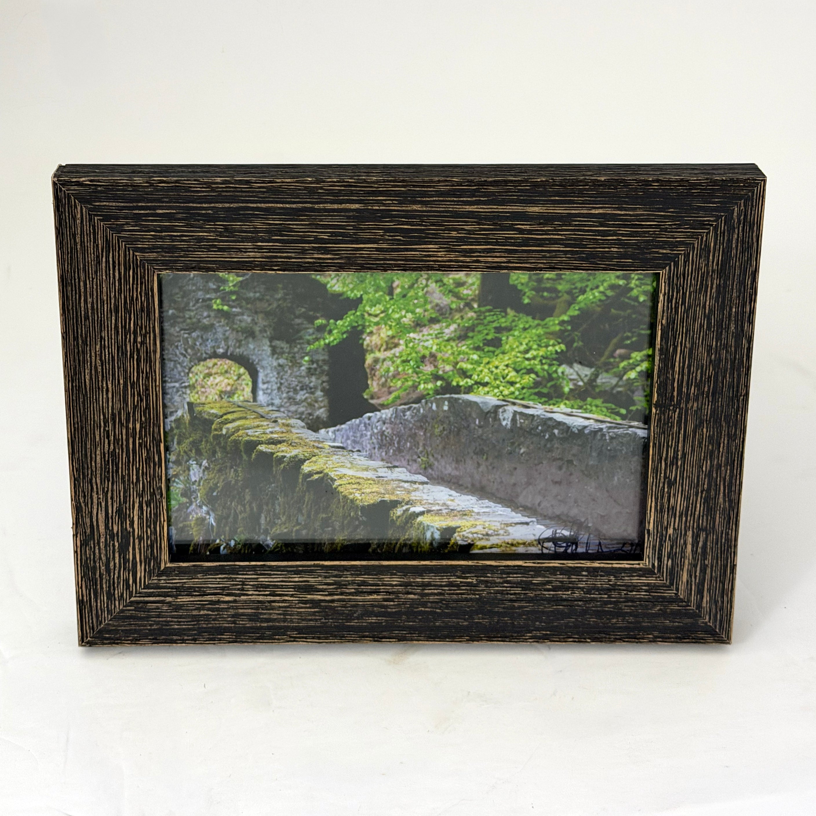 Stone bridge covered in moss in a forest in the Scottish Highlands, photo in a weather brown wood frame.