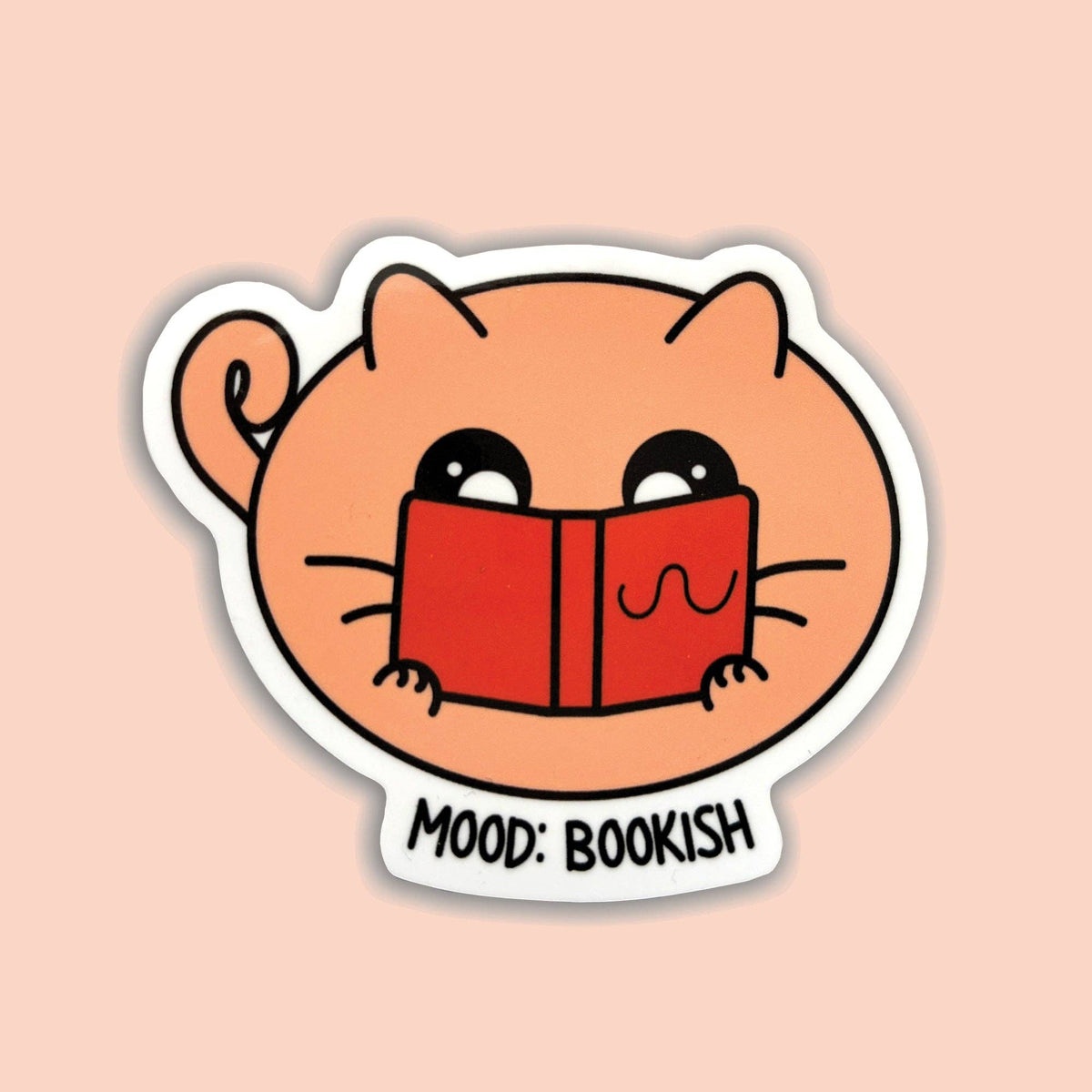 A die-cut sticker featuring a cute peach-colored cartoon cat holding a red book, with the text &