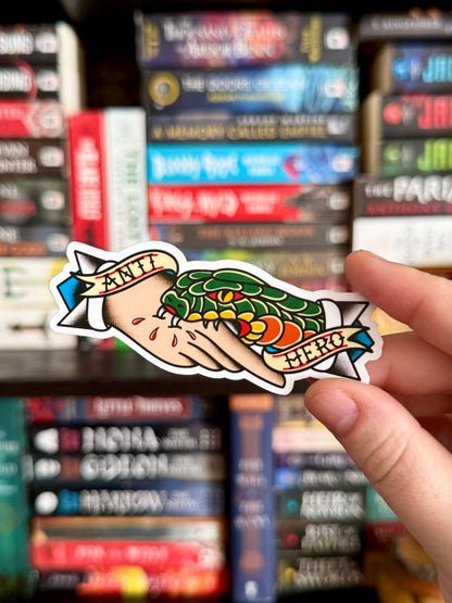 Hand holding a colorful sticker of a hand with a tattoo in front of book spines