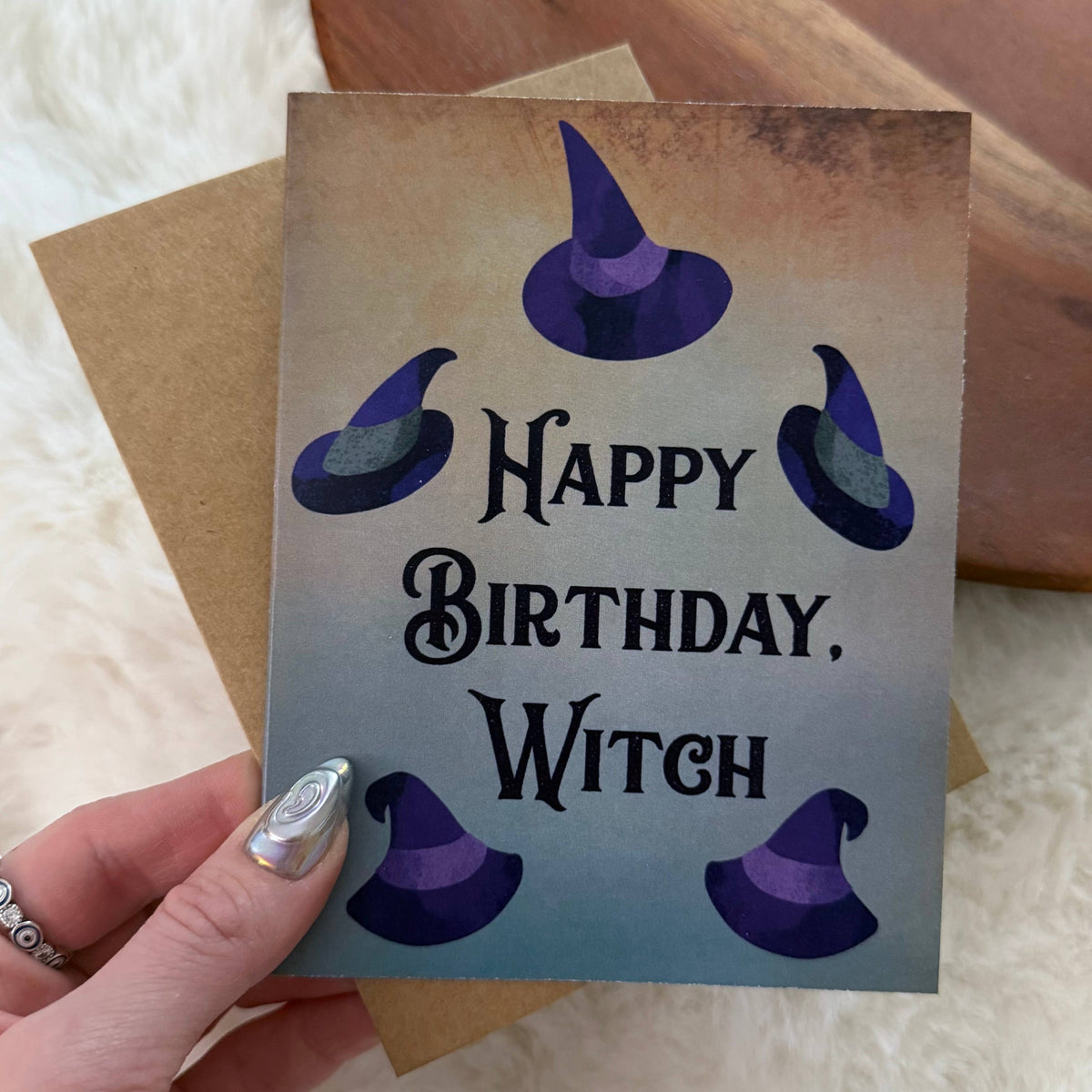 A hand holds a square birthday card that reads &