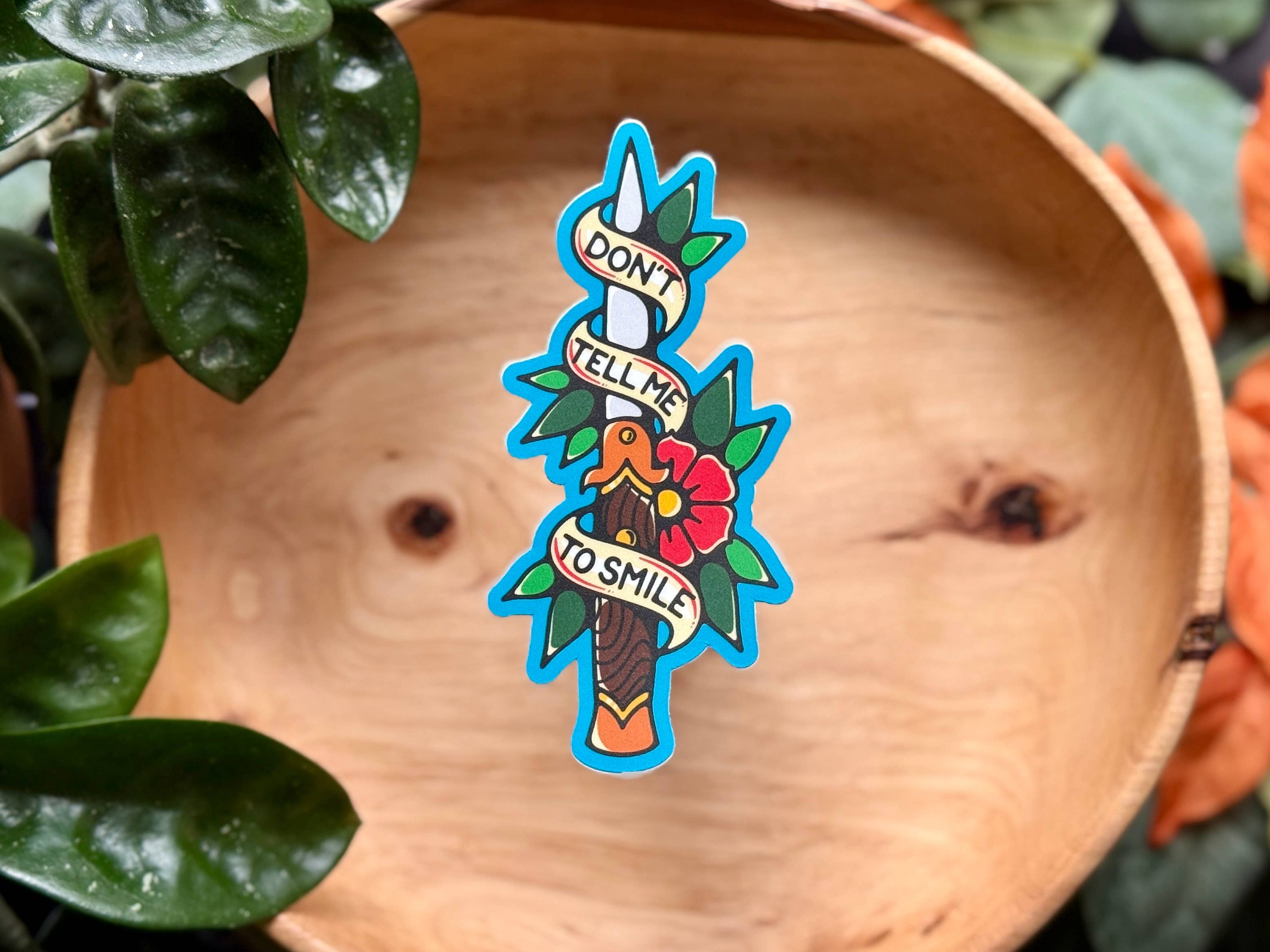 Colorful sticker with a parrot design on a wooden surface surrounded by green leaves.