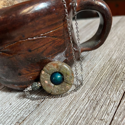 The Jasper Mood Bead Necklace | Color-Changing Mood Jewelry on Silver Chain is a handmade piece with a blue center pendant, shown resting against a rustic brown ceramic mug on a wooden surface.