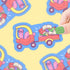 Cartoon character driving a car with books, surrounded by more similar stickers on a yellow background.