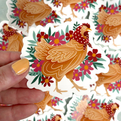 hand holding a sticker of a chicken wearing a polka dot handkerchief in front of flowers