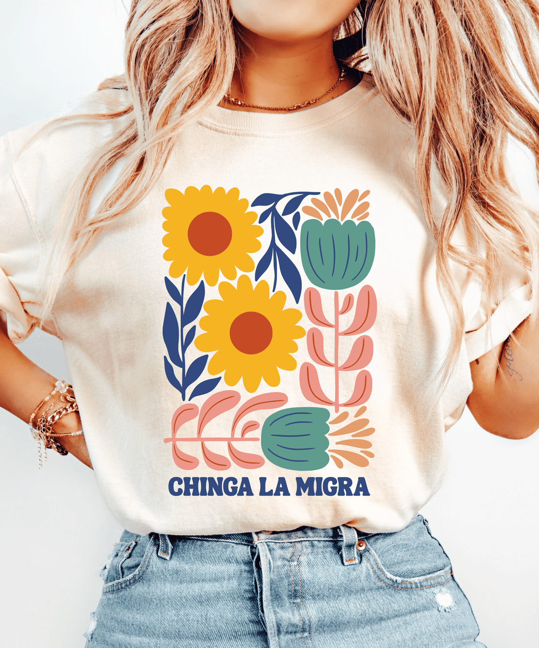 Ivory Chinga La Migra T-shirt with yellow flowers, pink and teal botanical artwork, and navy lettering.