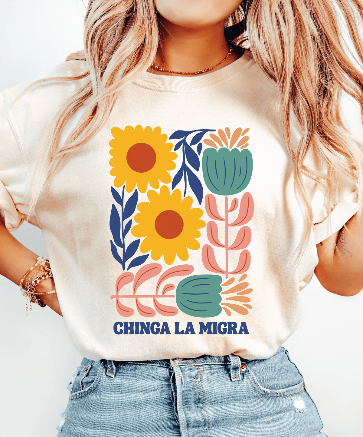Ivory Chinga La Migra T-shirt with yellow flowers, pink and teal botanical artwork, and navy lettering.