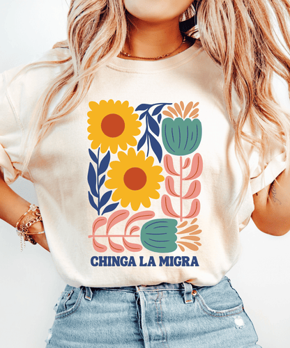 Ivory Chinga La Migra T-shirt with yellow flowers, pink and teal botanical artwork, and navy lettering.