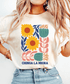 Ivory Chinga La Migra T-shirt with yellow flowers, pink and teal botanical artwork, and navy lettering.