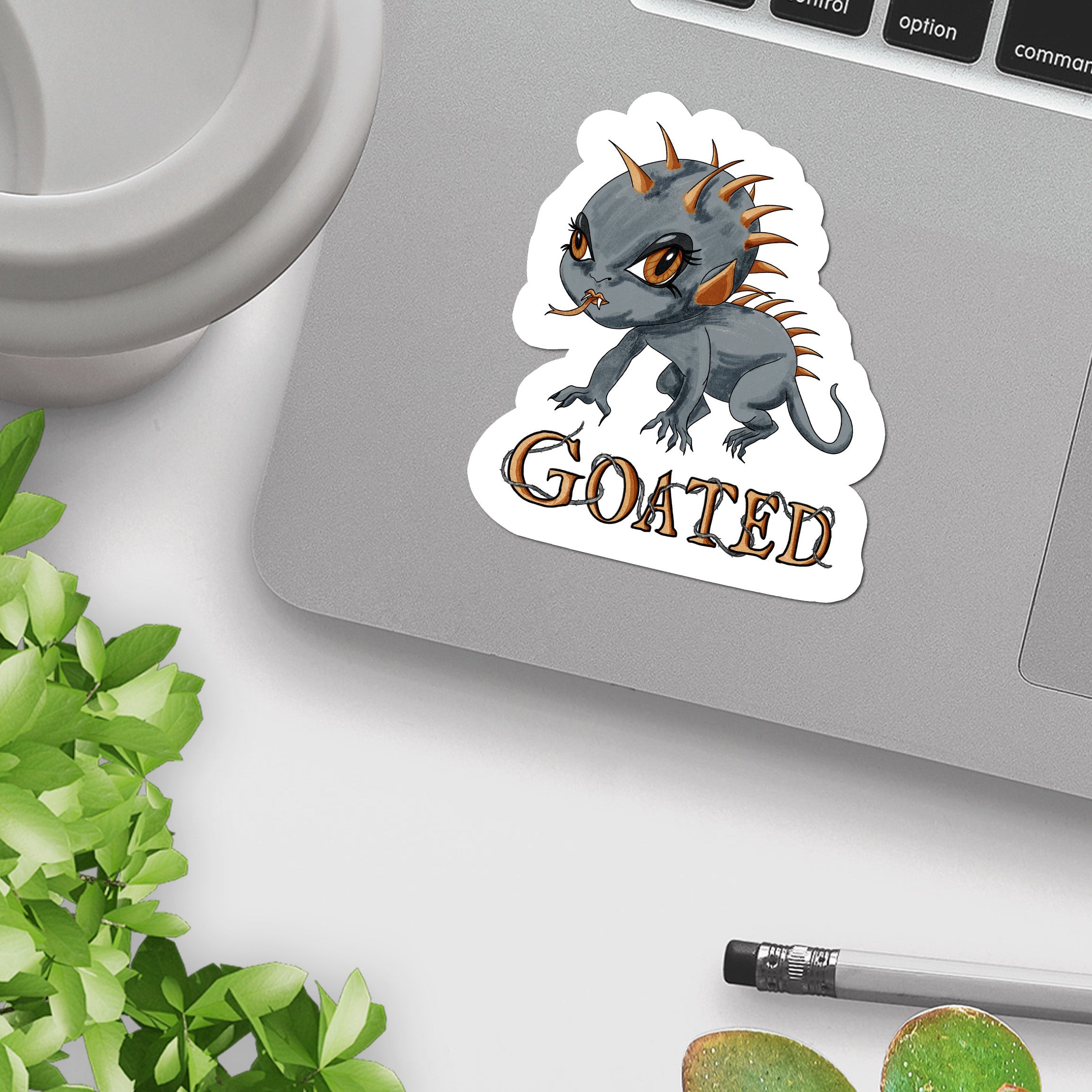 Creepy cute chupacabra sticker on a silver laptop beside a mug and green plant