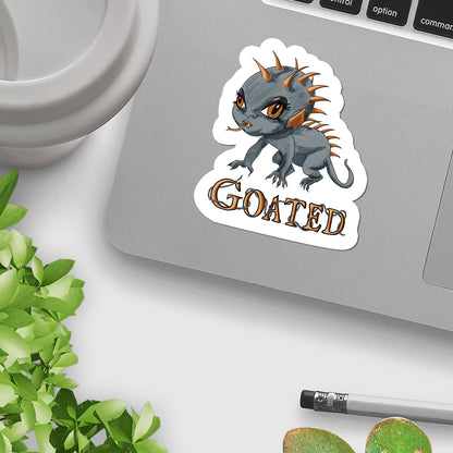 Creepy cute chupacabra sticker on a silver laptop beside a mug and green plant